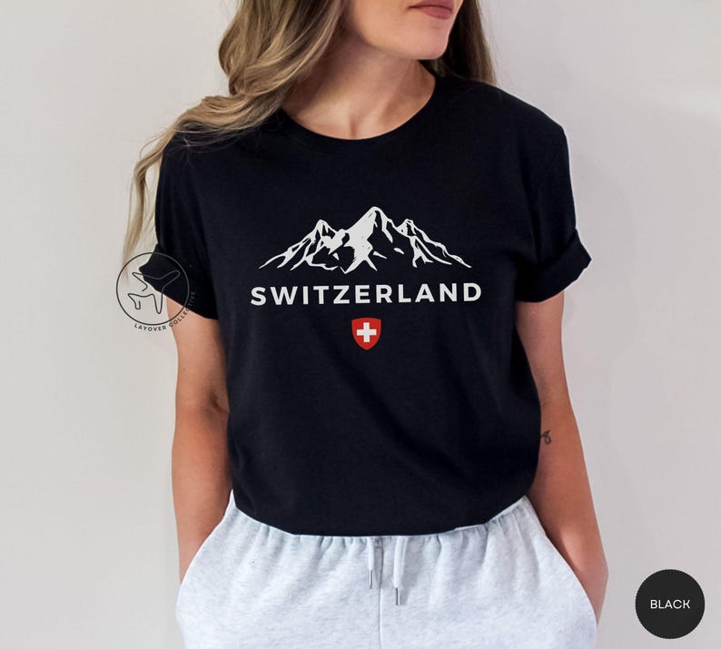 K&ouml;nnte beinhalten: Schwarzes T-Shirt mit wei&szlig;er Berglandschaft und dem Wort "SWITZERLAND". Darunter ein rot-wei&szlig;es Schweizer Kreuz. Das T-Shirt hat einen Rundhalsausschnitt.