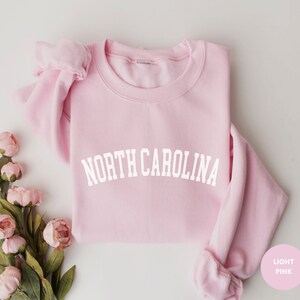 May include: A light pink sweatshirt with the text "NORTH CAROLINA" in white lettering.