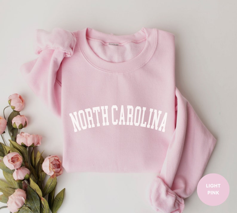 May include: A light pink sweatshirt with the text "NORTH CAROLINA" in white lettering.