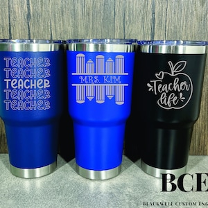 May include: Three stainless steel tumblers with different teacher-themed designs. The first tumbler is blue with the word "Teacher" repeated five times. The second tumbler is blue with a design of pencils and the text "Mrs. Kim". The third tumbler is black with an apple and the text "Teacher life".