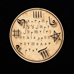 May include: A circular beige disc featuring dark brown markings, including a five-pointed star, a hashtag symbol, and various Arabic numerals and script characters arranged in rows. The surface has a weathered, parchment-like texture.