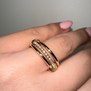 May include: A gold ring with three bands, one of which is set with small clear stones.