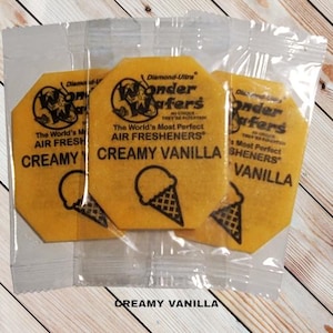 May include: Three yellow octagonal air freshener wafers with the text "Wonder Wafers" and "The World's Most Perfect Air Fresheners" in black. The wafers are labeled "Creamy Vanilla".