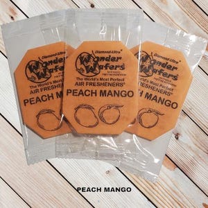 May include: Three octagonal air freshener wafers in individual plastic pouches. Each wafer is orange and features a peach and mango design. The text "Wonder Wafers" is printed on each wafer, along with the phrase "The World's Most Perfect Air Fresheners".