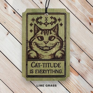 May include: A wooden sign with a green background and a black cat with a mischievous grin. The sign reads "Cat-titude is Everything." and "Lime Grass" at the bottom.