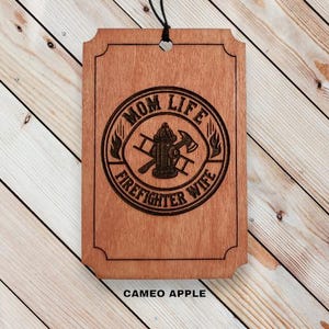 May include: Wooden sign with a brown stain and rounded corners. The sign has a circle with the text "Mom Life Firefighter Wife" and a fire hydrant with crossed axes inside the circle.
