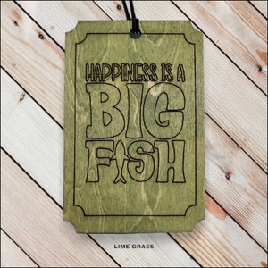 May include: A wooden sign with a green stain and black lettering that reads "Happiness is a Big Fish". The sign has a rope hanger and the words "Lime Grass" are printed at the bottom.