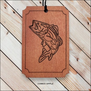 May include: A wooden cutout of a bass fish with a black outline. The cutout is on a brown wooden background. The text "CAMEO APPLE" is printed below the cutout.