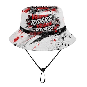 May include: A white bucket hat featuring a red and black graphic print with tire tracks, paint splatters, and dice. The text reads VEGAS RYDERZ EST 2021. It includes a black chin strap with an adjustable toggle for a secure fit around the head.