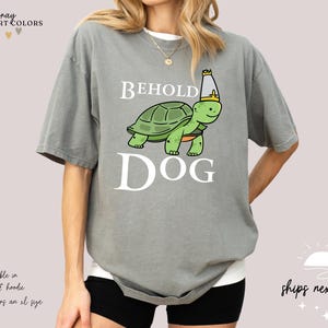 May include: Grey t-shirt featuring a cartoon turtle wearing a crown and the text "Behold Dog".