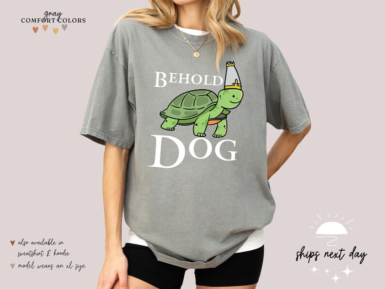 May include: Grey t-shirt featuring a cartoon turtle wearing a crown and the text "Behold Dog".
