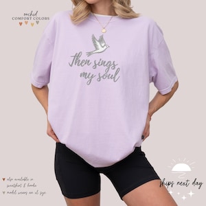 Puede incluir: Una camiseta lavanda con una paloma blanca y el texto "Then sings my soul".