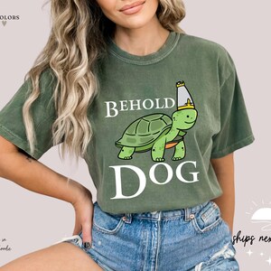 May include: A green t-shirt with a white graphic of a turtle wearing a crown and the text "BEHOLD DOG".
