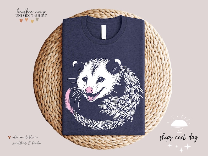 Puede incluir: Camiseta unisex azul marino jaspeado con un dise&ntilde;o de zarig&uuml;eya en blanco y negro, con nariz y cola rosas. El texto "heather navy" y "UNISEX T-SHIRT" est&aacute;n en la parte superior. Tambi&eacute;n disponible en sudadera y sudadera con capucha.