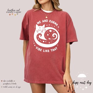 K&ouml;nnte beinhalten: Unisex-T-Shirt in der Farbe Heather Red mit einem wei&szlig;en Grafikdruck eines Katzen, das sich in einem Kreis zusammenrollt, mit dem Text "Me and Karma Vibe Like That".