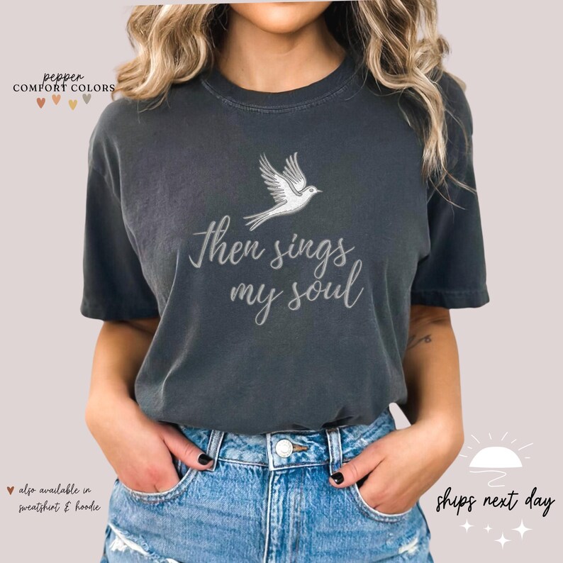 Puede incluir: Una camiseta gris oscuro con una paloma blanca y el texto "Then sings my soul" impreso en la parte delantera.