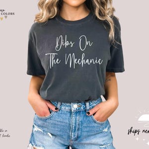 May include: A dark gray t-shirt with the text "Dibs On The Mechanic" in white lettering.