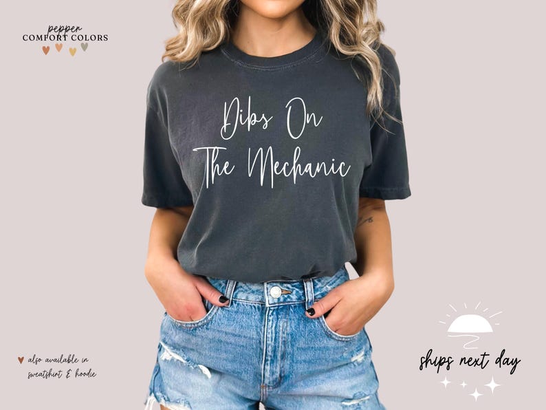 May include: A dark gray t-shirt with the text "Dibs On The Mechanic" in white lettering.