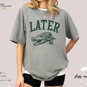 a woman wearing a gray shirt with a green alligator on it