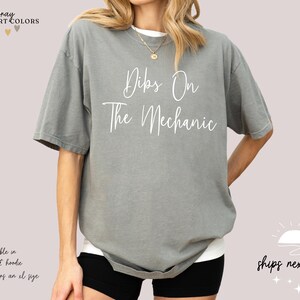 May include: Gray t-shirt with the text "Dibs On The Mechanic" in white lettering.