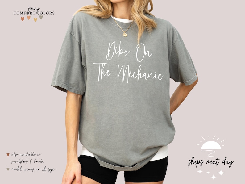 May include: Gray t-shirt with the text "Dibs On The Mechanic" in white lettering.
