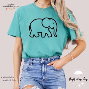 May include: A teal blue t-shirt with a black outline of an elephant. The text "Seafoam Comfort Colors" is at the top of the shirt.