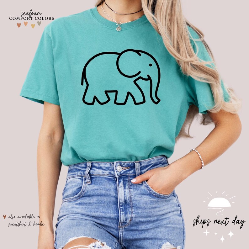 May include: A teal blue t-shirt with a black outline of an elephant. The text "Seafoam Comfort Colors" is at the top of the shirt.