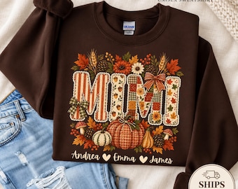 May include: A dark brown crewneck sweatshirt featuring the word MIMI in large, patterned block letters surrounded by autumn leaves, pumpkins, pinecones, and mushrooms. The names Andrea, Emma, and James are printed below with heart icons.