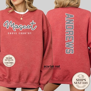 May include: A heathered red crewneck sweatshirt featuring the white text Mascot Cross Country on the front and the vertical white text ANDREWS on the back. The garment has long sleeves and a ribbed collar, cuffs, and hem, showcasing a casual design.