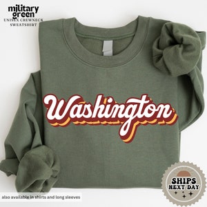 May include: A military green sweatshirt with the word "Washington" in a retro, multi-colored font.