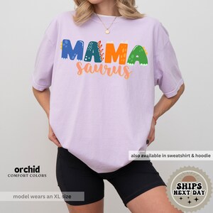 a woman wearing a purple shirt with the word mamasaurus on it