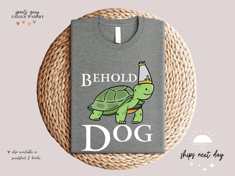 May include: A grey t-shirt featuring a cartoon turtle wearing a crown and the text "BEHOLD DOG" printed on it.