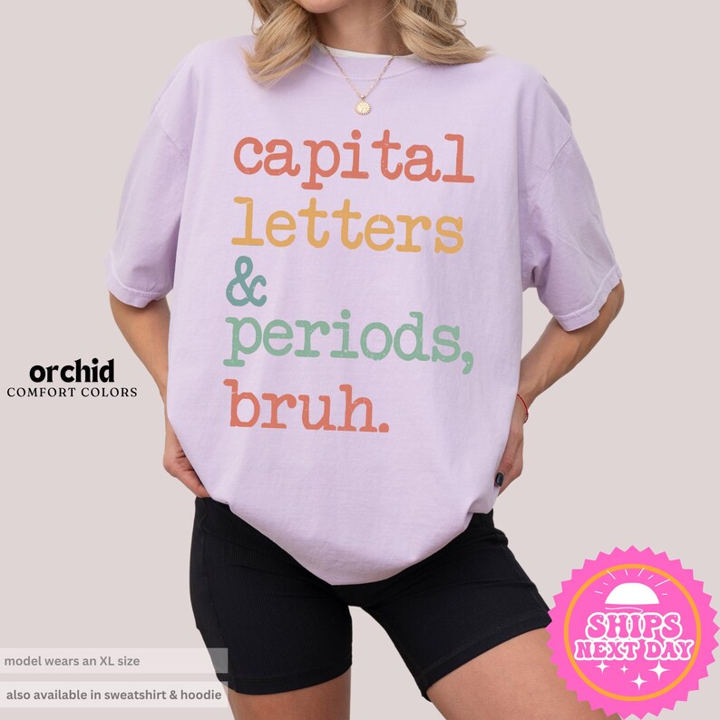 K&ouml;nnte beinhalten: Ein helles lila T-Shirt mit dem Text "capital letters & periods, bruh." in Regenbogenfarben.