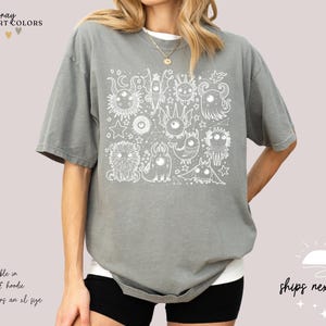 May include: Gray t-shirt with a white graphic of a group of cartoon monsters. The text "gray COMFORT COLORS" is at the top of the image.