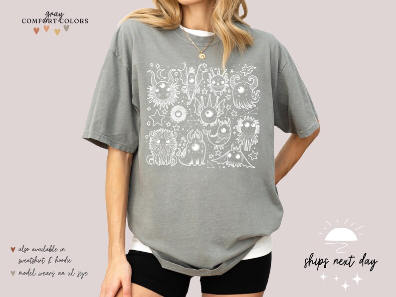 May include: Gray t-shirt with a white graphic of a group of cartoon monsters. The text "gray COMFORT COLORS" is at the top of the image.