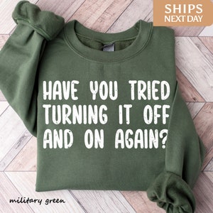 May include: A military green sweatshirt with the text "HAVE YOU TRIED TURNING IT OFF AND ON AGAIN?" printed in white.