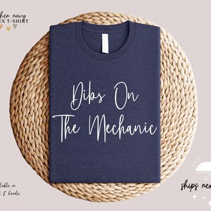 May include: A heather navy unisex t-shirt with the text "Dibs On The Mechanic" printed in white.