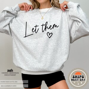 May include: Gray sweatshirt with the text "Let them" in black cursive lettering and a small heart.