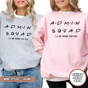 May include: Two sweatshirts, one gray and one pink, each with the text "ADMIN SQUAD" in black letters with colorful dots, and the phrase "I'LL BE THERE FOR YOU" below. The gray sweatshirt has the text "MORE STYLES + COLORS" at the bottom.