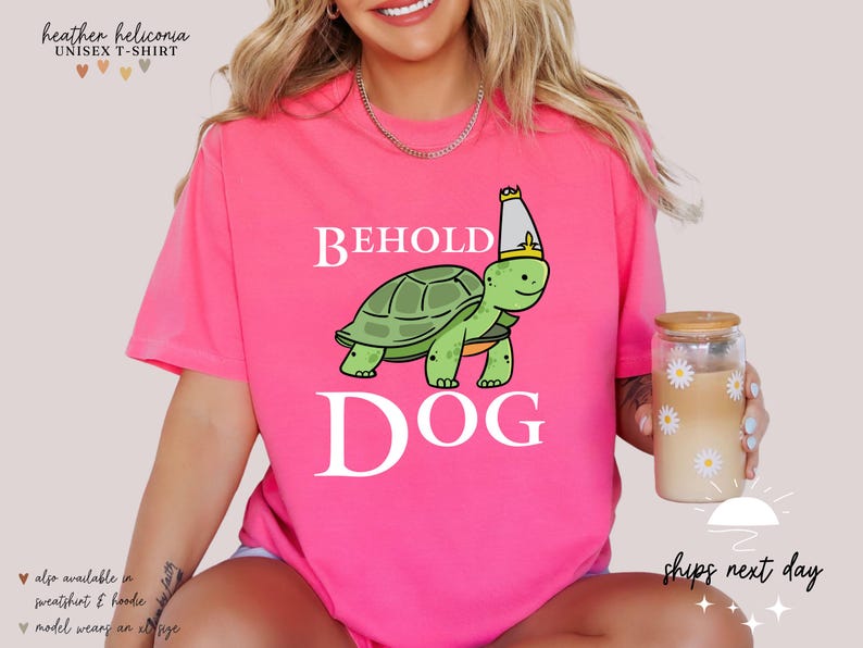 May include: Pink t-shirt featuring a white graphic of a turtle wearing a crown and the text "Behold Dog".