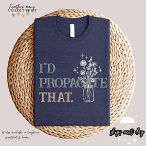 Puede incluir: Camiseta unisex azul marino jaspeado con el texto "I'D PROPAGATE THAT" y una ilustraci&oacute;n floral en un tarro de cristal. La camiseta se muestra sobre una esterilla tejida. Tambi&eacute;n disponible en sudadera y sudadera con capucha de manga larga.