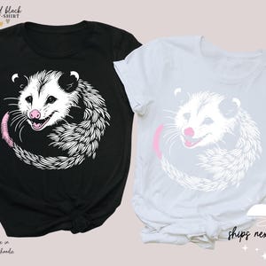 Puede incluir: Dos camisetas unisex, una negra y otra blanca, con un dise&ntilde;o de zarig&uuml;eya. La zarig&uuml;eya tiene la cara blanca, la nariz rosa y la cola rosa. El texto "white and black" y "UNISEX T-SHIRT" est&aacute; en la parte superior. El texto "ships next day" est&aacute; en la parte inferior.