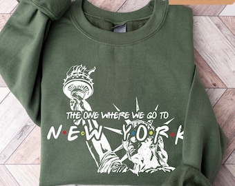 May include: A green sweatshirt with a white graphic of the Statue of Liberty and the text "The One Where We Go To New York".