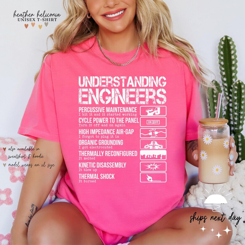May include: Pink t-shirt with white text that reads "Understanding Engineers" and a list of humorous engineering terms. The terms include "Percussive Maintenance", "Cycle Power to the Panel", "High Impedance Air-Gap", "Organic Grounding", "Thermally Reconfigured", "Kinetic Disassembly", and "Thermal Shock".