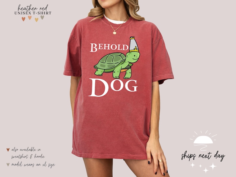 May include: A heather red unisex t-shirt featuring a cartoon turtle wearing a crown and the text "BEHOLD DOG".