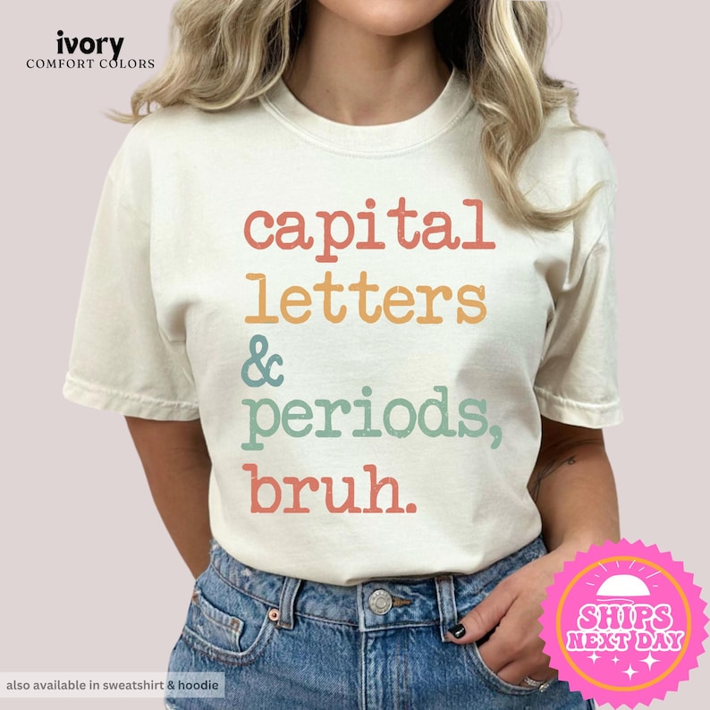 K&ouml;nnte beinhalten: Ein wei&szlig;es T-Shirt mit dem Text "capital letters & periods, bruh." in einer Retro-Schriftart mit bunten Akzenten.