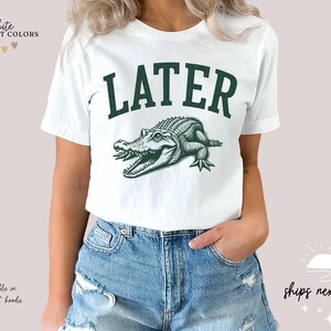 a woman wearing a white shirt with a green alligator on it