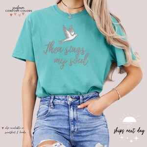 Puede incluir: Una camiseta azul turquesa con una paloma blanca y el texto "Then sings my soul" en gris.