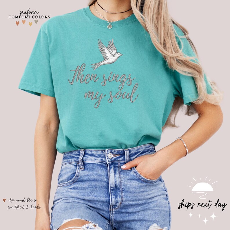 Puede incluir: Una camiseta azul turquesa con una paloma blanca y el texto "Then sings my soul" en gris.