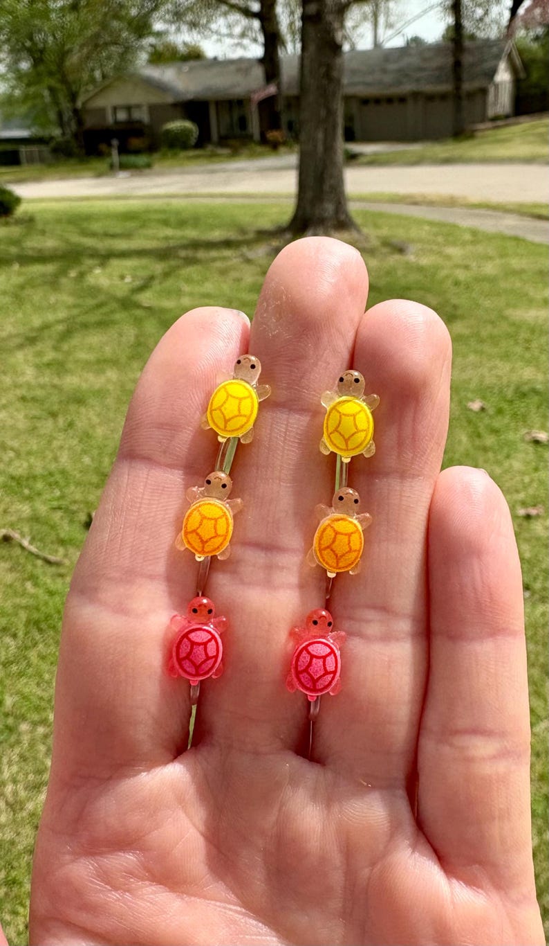 Puede incluir: Un juego de seis pinzas para el pelo de tortuga de colores. Las pinzas est&aacute;n hechas de pl&aacute;stico y tienen un acabado brillante. Las tortugas est&aacute;n dispuestas en un degradado de amarillo a naranja a rosa.